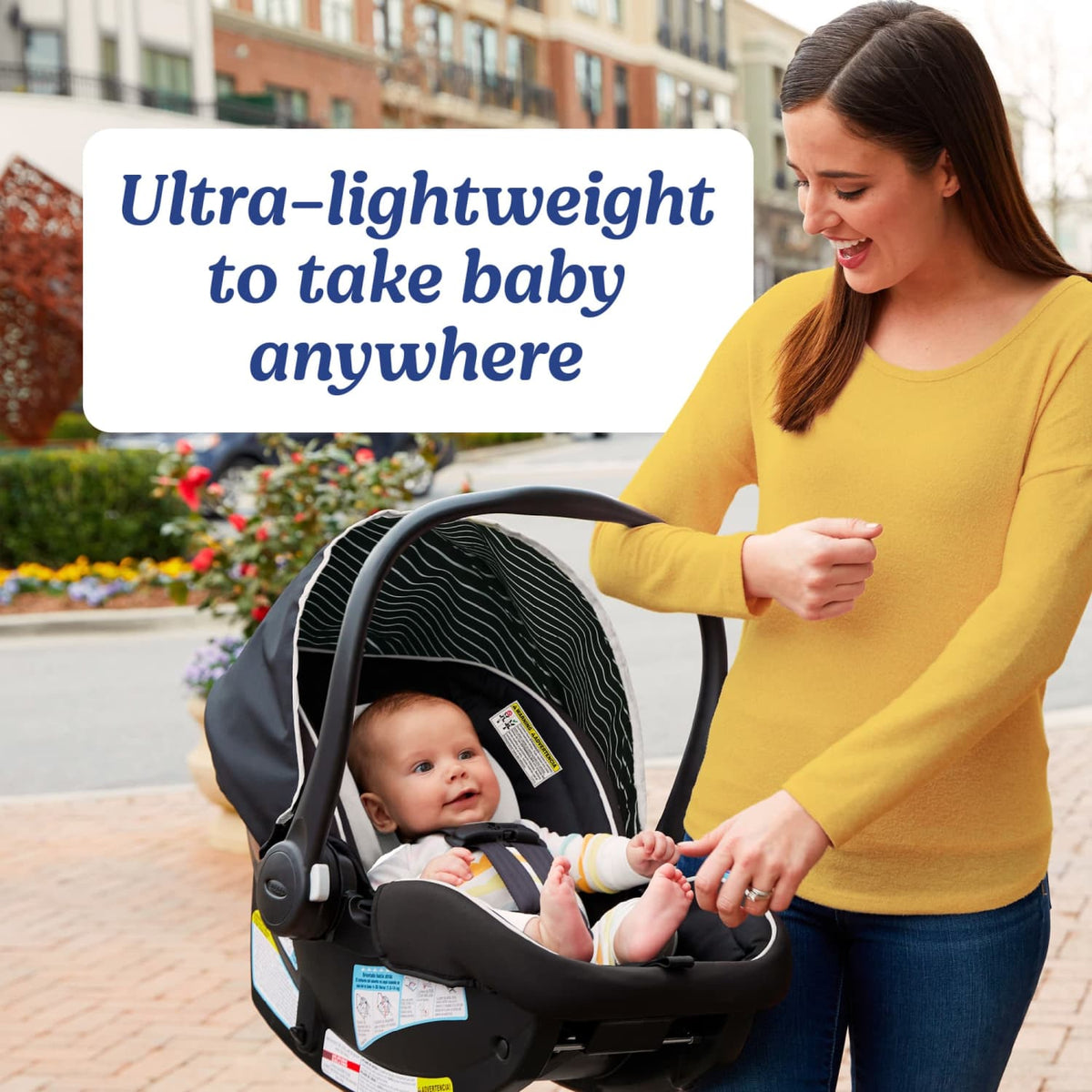 An image of a smiling woman caretaker in a yellow shirt holding a black Graco Snugride Lite XL Infant Car Seat with a baby inside the seat. Graphic text on the image reads "Ultra-lightweight to take baby anywhere."
