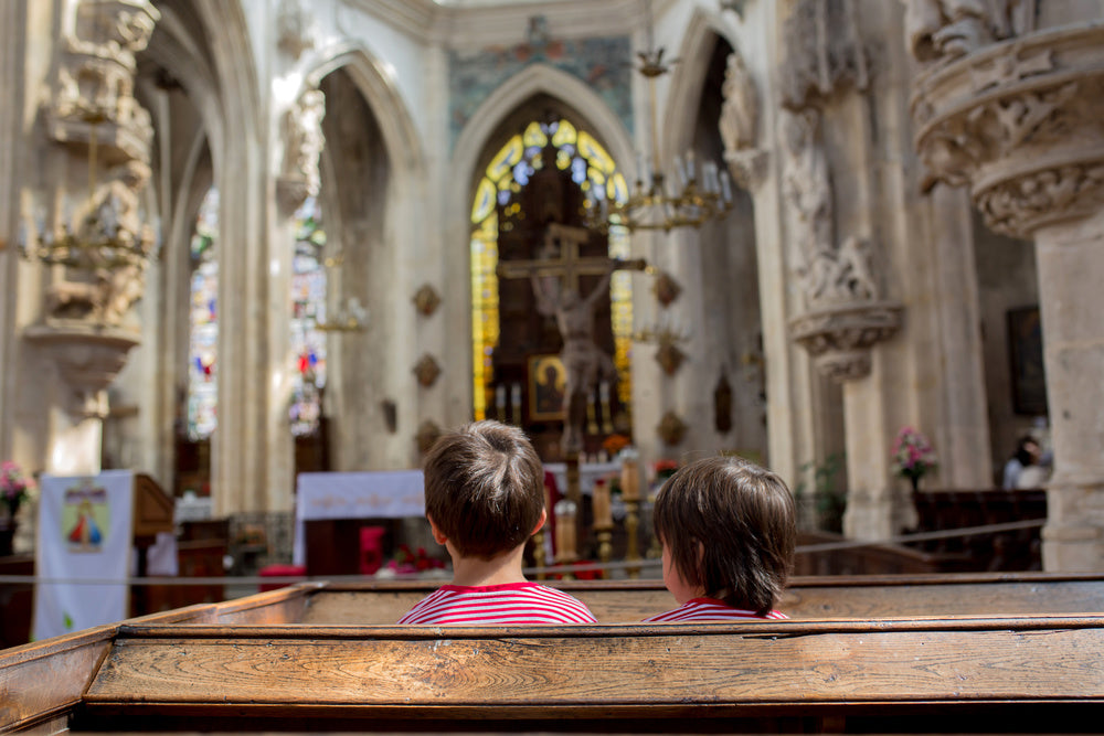 Two children sitting in a church pew facing the altar.