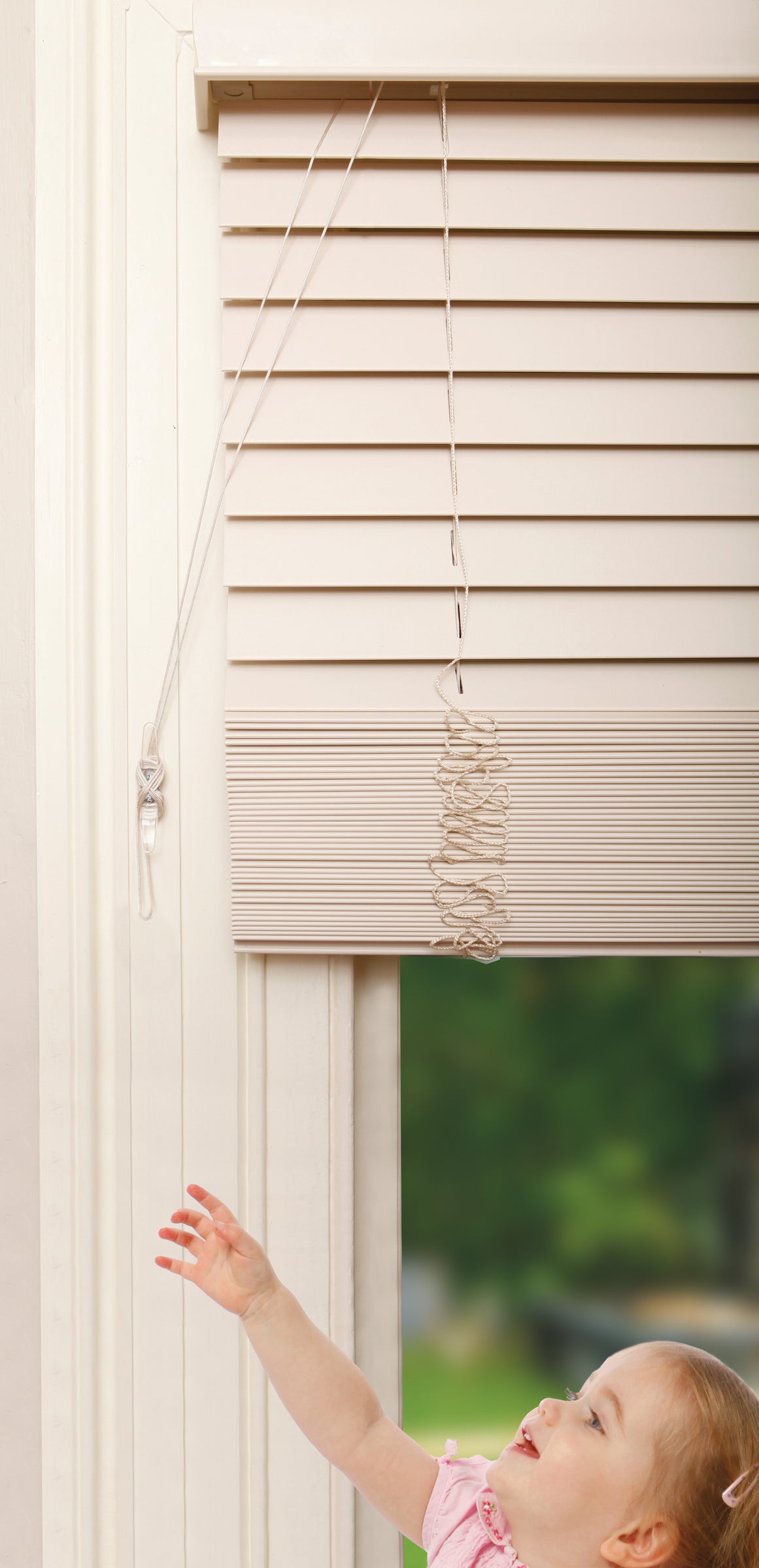 Child reaching out to touch a window blind with a blurred outdoor background
