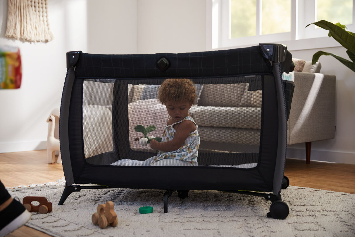 Child playing with a toy inside a portable playpen in a living room.