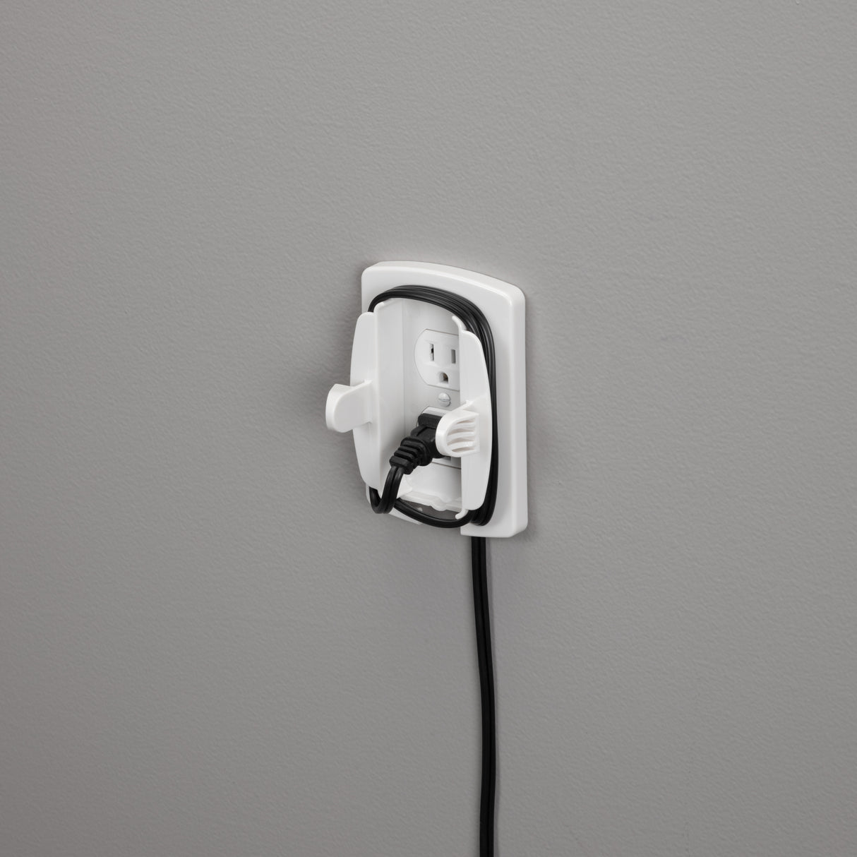 Wall-mounted electrical outlet with a black cord plugged into it on a gray background