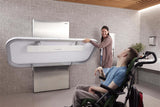 Person using a modern bathroom facility with a wheelchair and another person assisting.