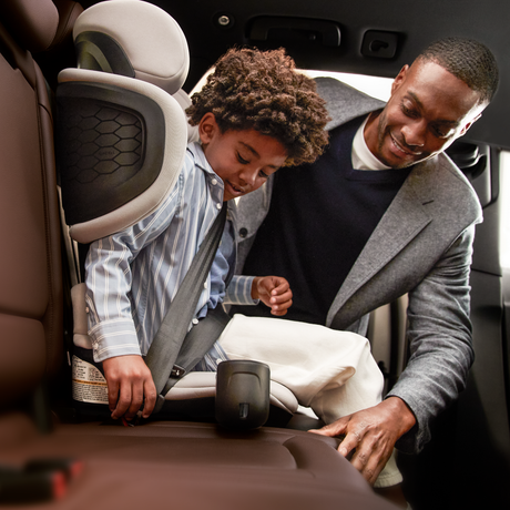 Man and child in a car, with the child being buckled into a car seat.