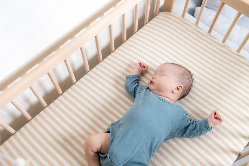 Baby lying on a striped crib sheet in a wooden crib