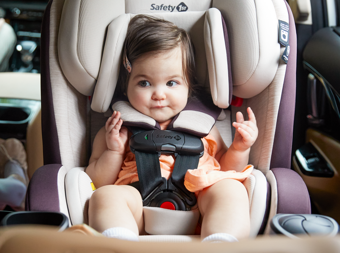 Child in a car seat with a visible Safety 1st logo, inside a vehicle.