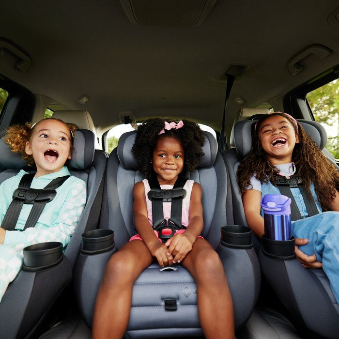 Three children in car seats with safety belts, smiling and laughing inside a vehicle.