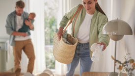 Family of three in a home setting with a woman holding a bag and a baby being held by a man.
