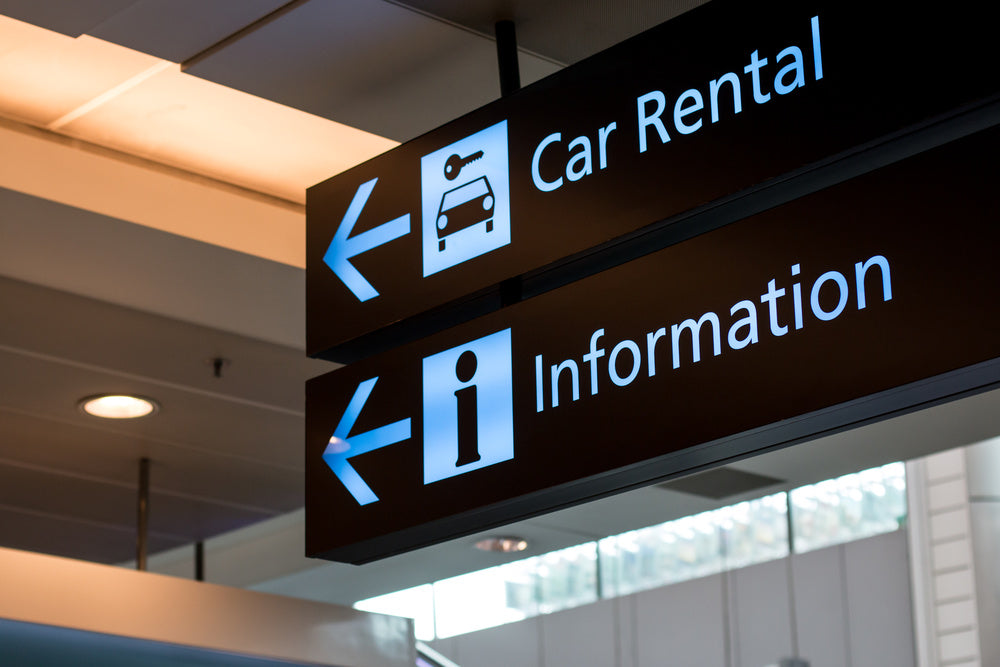 Directional signs pointing to car rental and information in an indoor setting.
