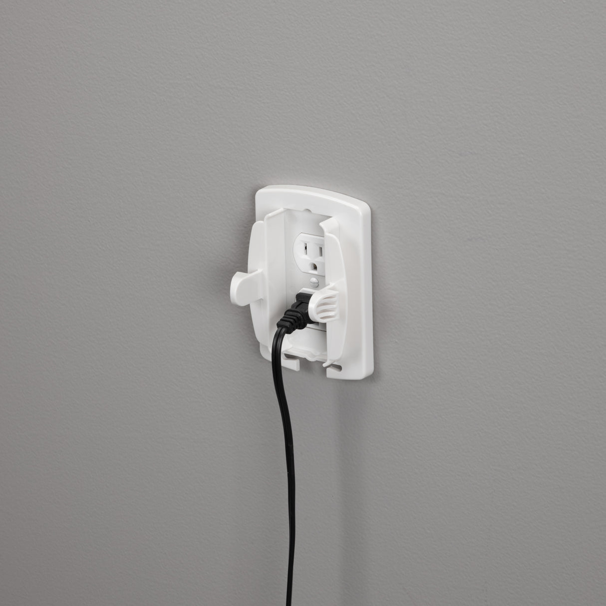 White electrical outlet with a black cord plugged in on a gray wall